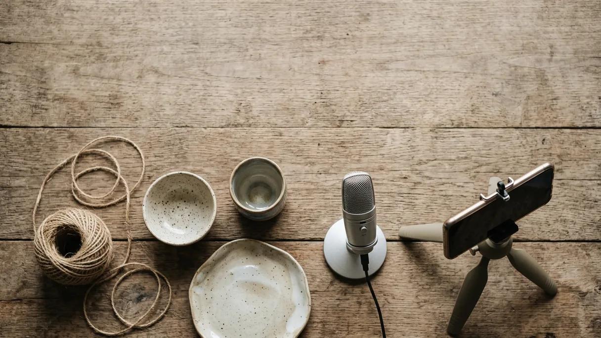 A workbench with ceramics, twine, a microphone, and a phone on a tripod aimed at the work.