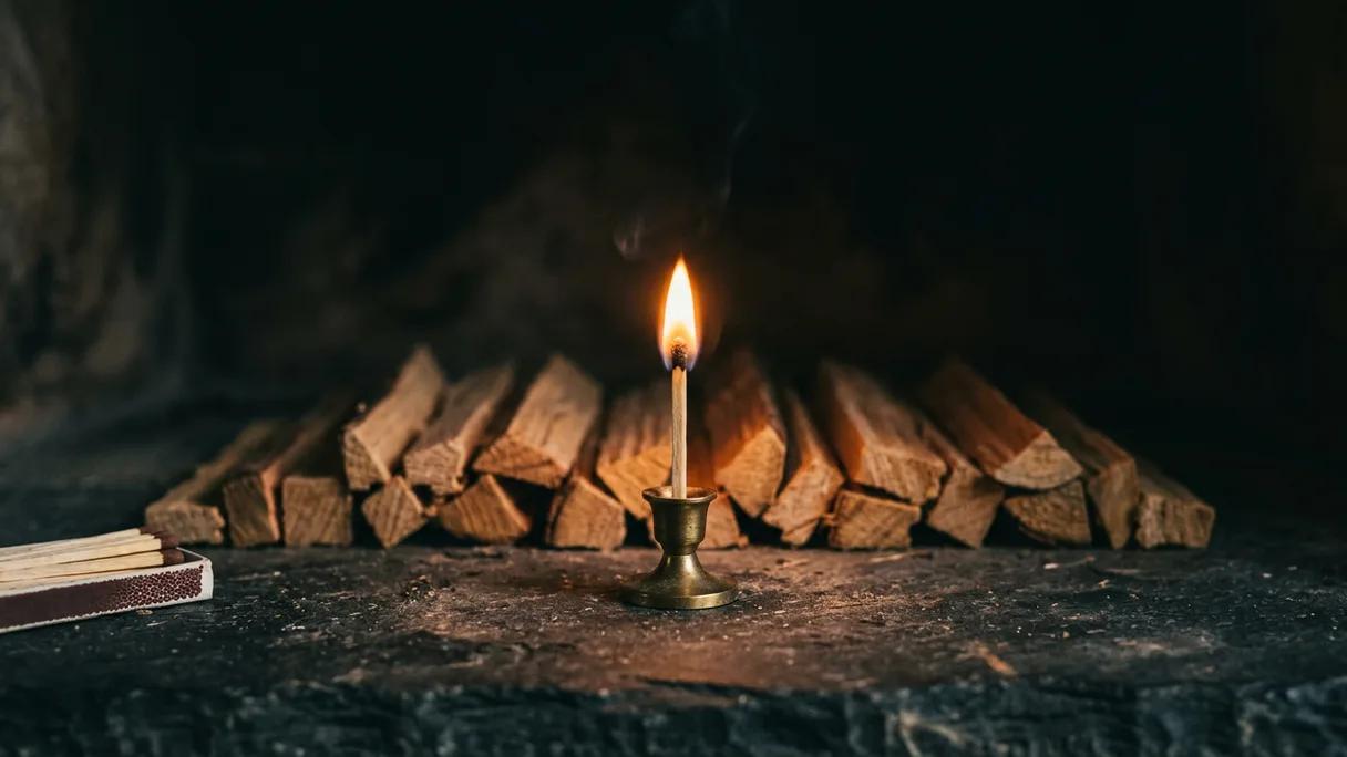 A single lit match above a small stack of kindling on slate, glowing in soft dim light.
